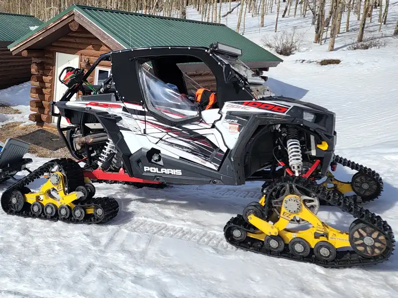 Polaris RZR 1000 fitted with yellow Mattracks EZ-series tracks, outside a log cabin in winter